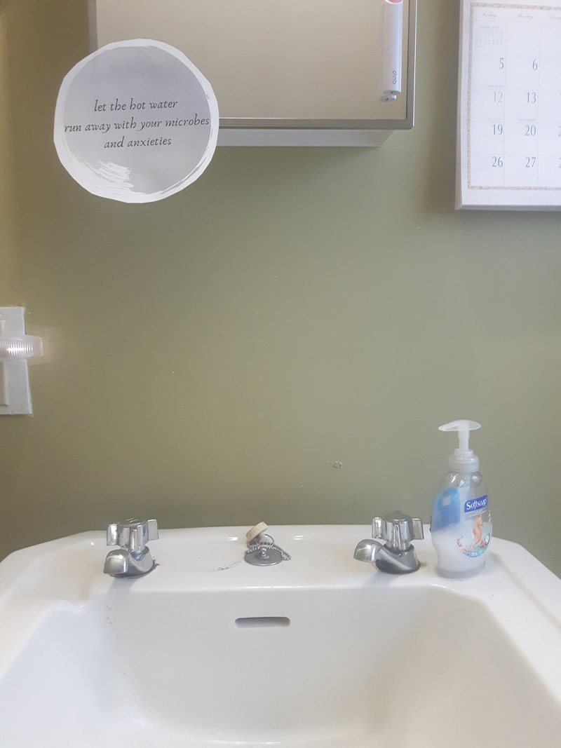 A white bathroom sink, with a poem in a blue bubble taped to the mirror above it.